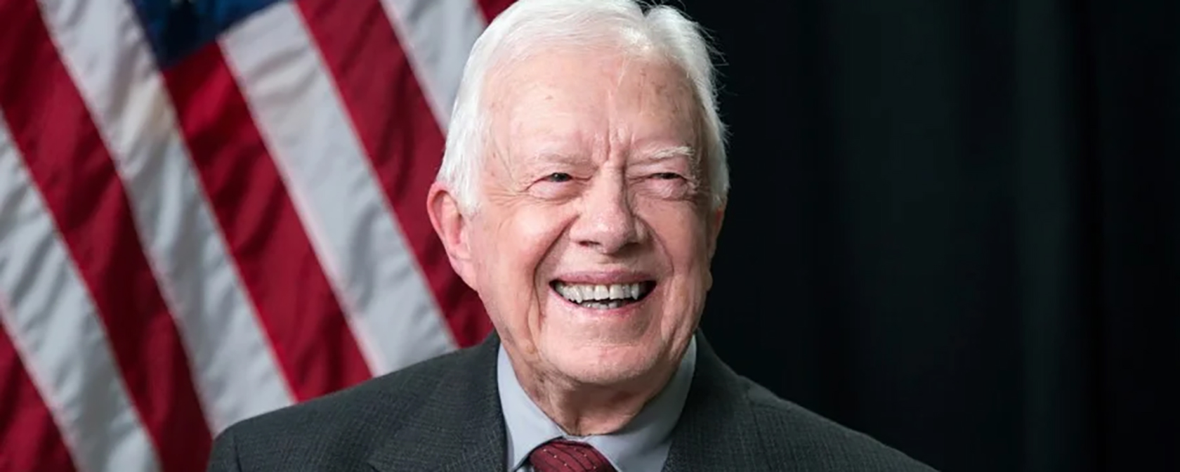 President Jimmy Carter smiling in front of a flag